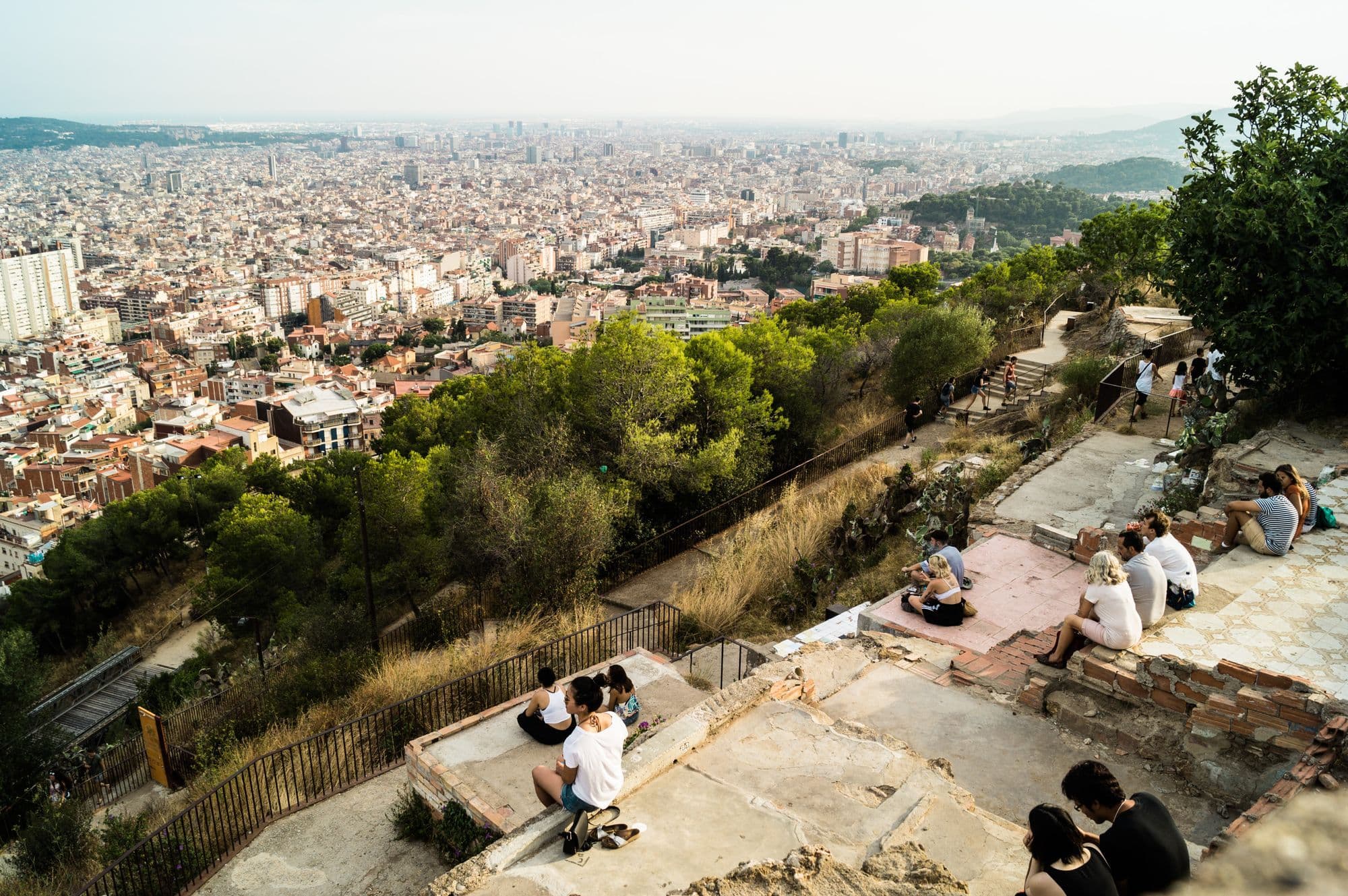 Visitors sitting on the concrete platforms of the Bunkers del Carmel with Barcelona's rooftops stretching to the sea below.