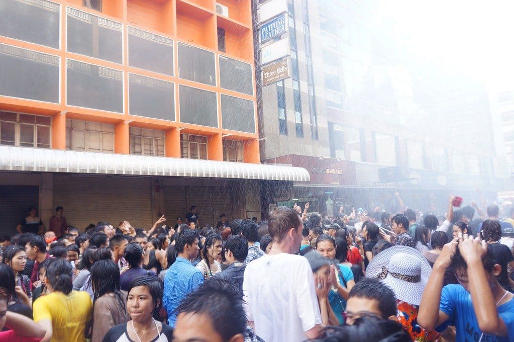A soaked crowd celebrating Songkran on Silom Road, water raining down in front of the Patpong Leather sign.