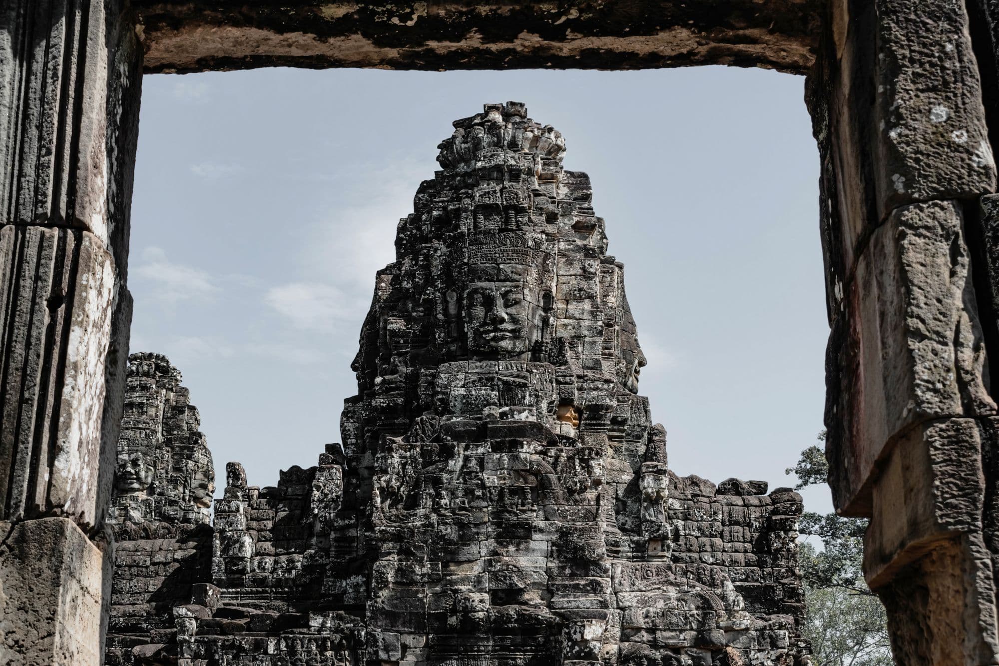 A tower carved with a serene stone face at the Bayon, framed by a dark stone doorway against a pale sky.