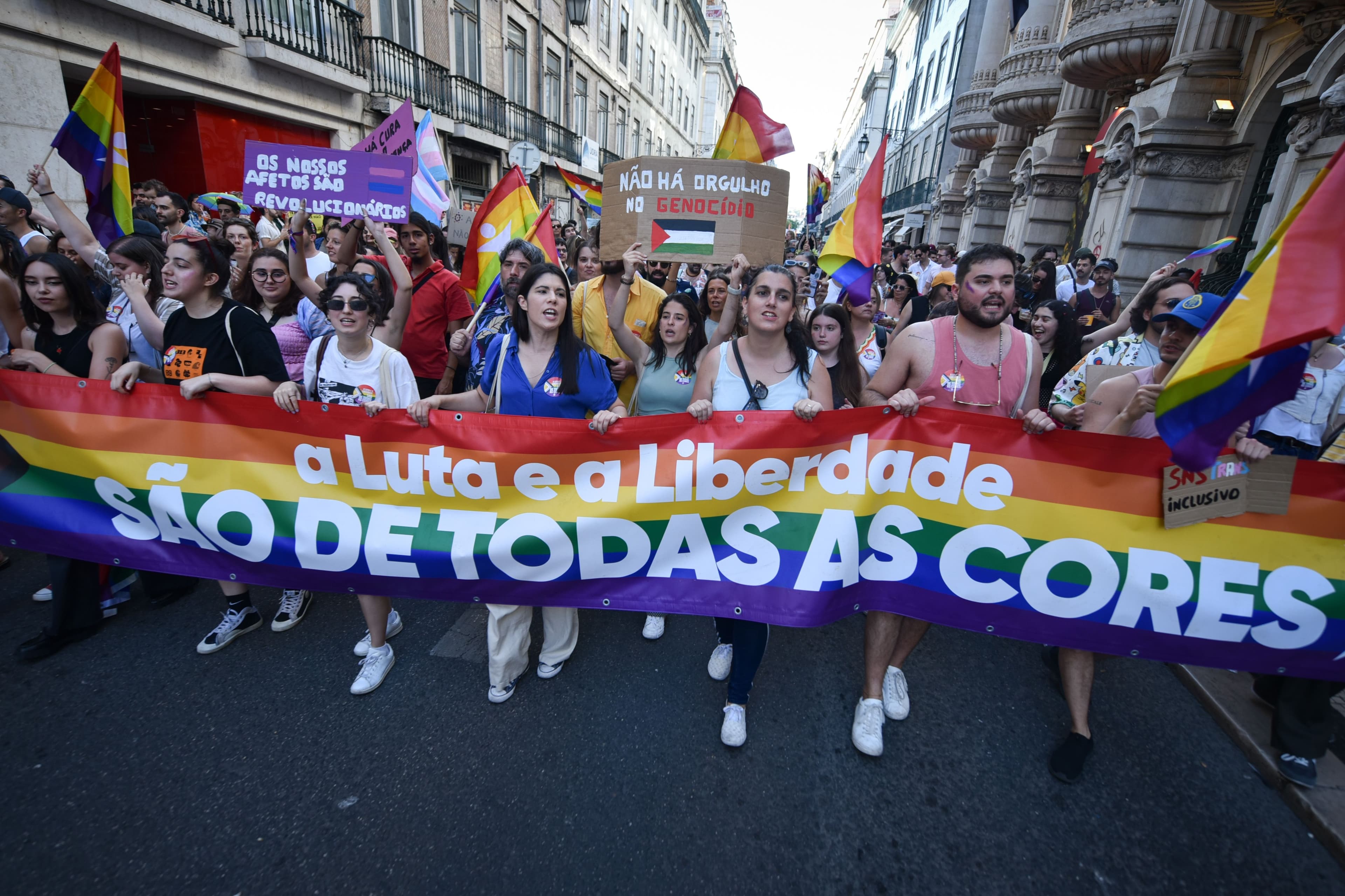 Marchers under rainbow flags carry a wide rainbow banner at the front of the Lisbon Pride March in June 2023.
