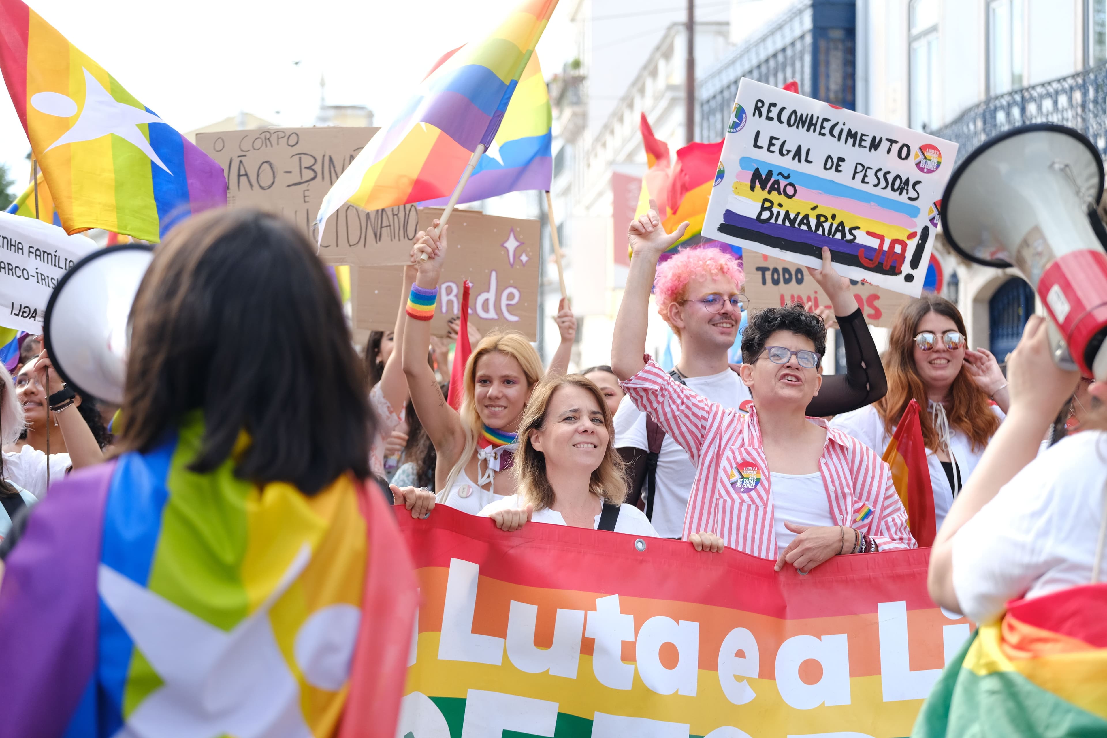Marchers with rainbow flags and handmade signs behind a banner at the Lisbon LGBTI+ Pride March in June 2022.