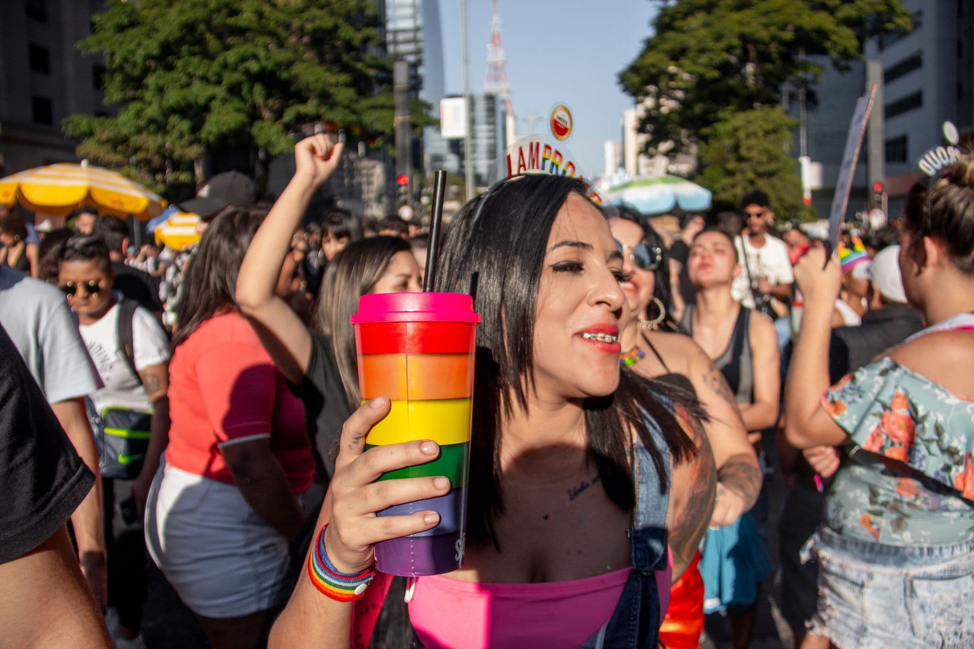 Pride marchers carrying rainbow flags along a packed São Paulo avenue in daylight.