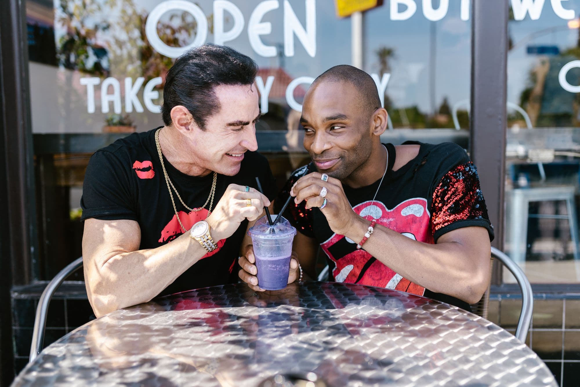 Two men sharing a drink and laughing at an outdoor café table.