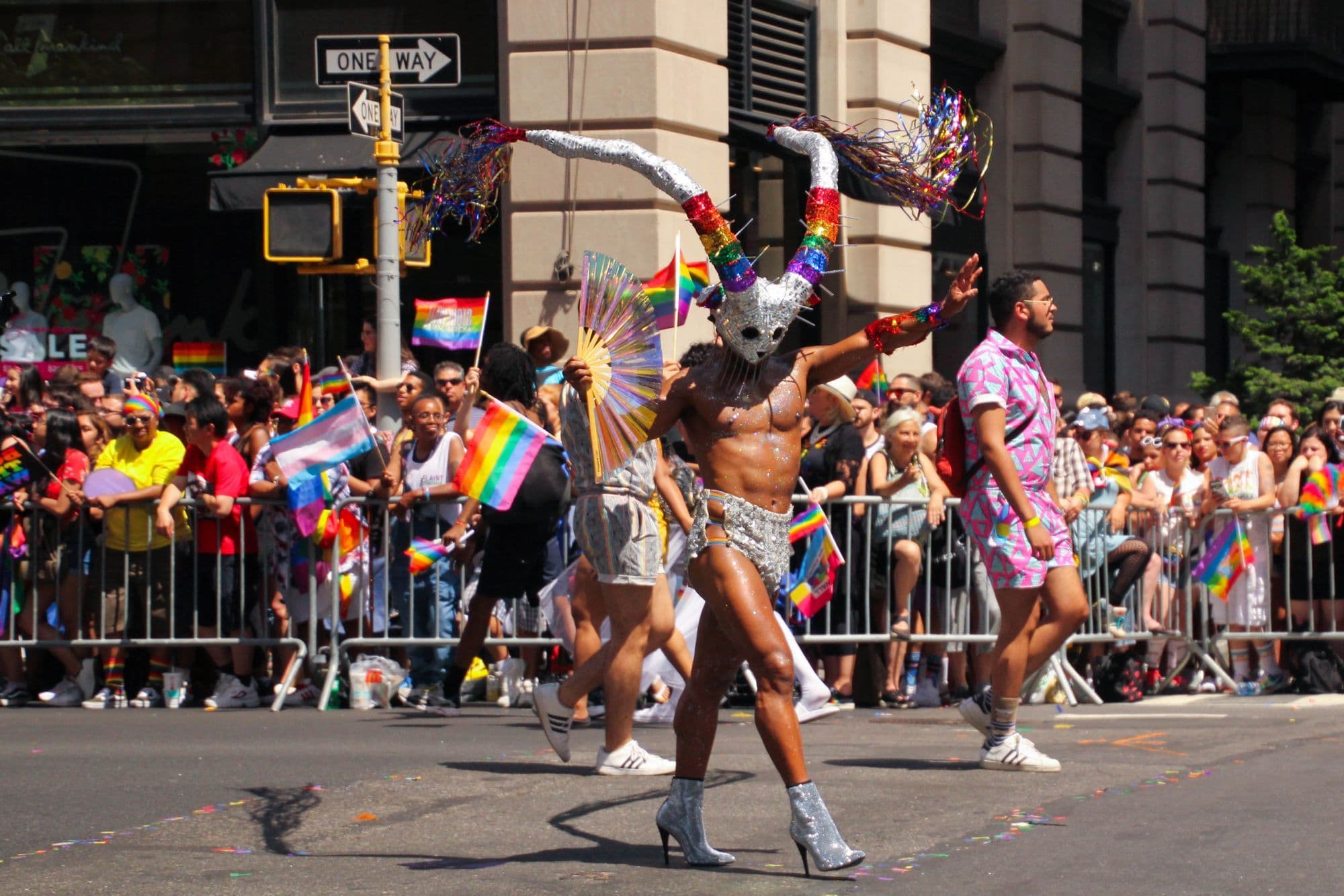 Performers in colourful outfits and rainbow flags move through New York City Pride.