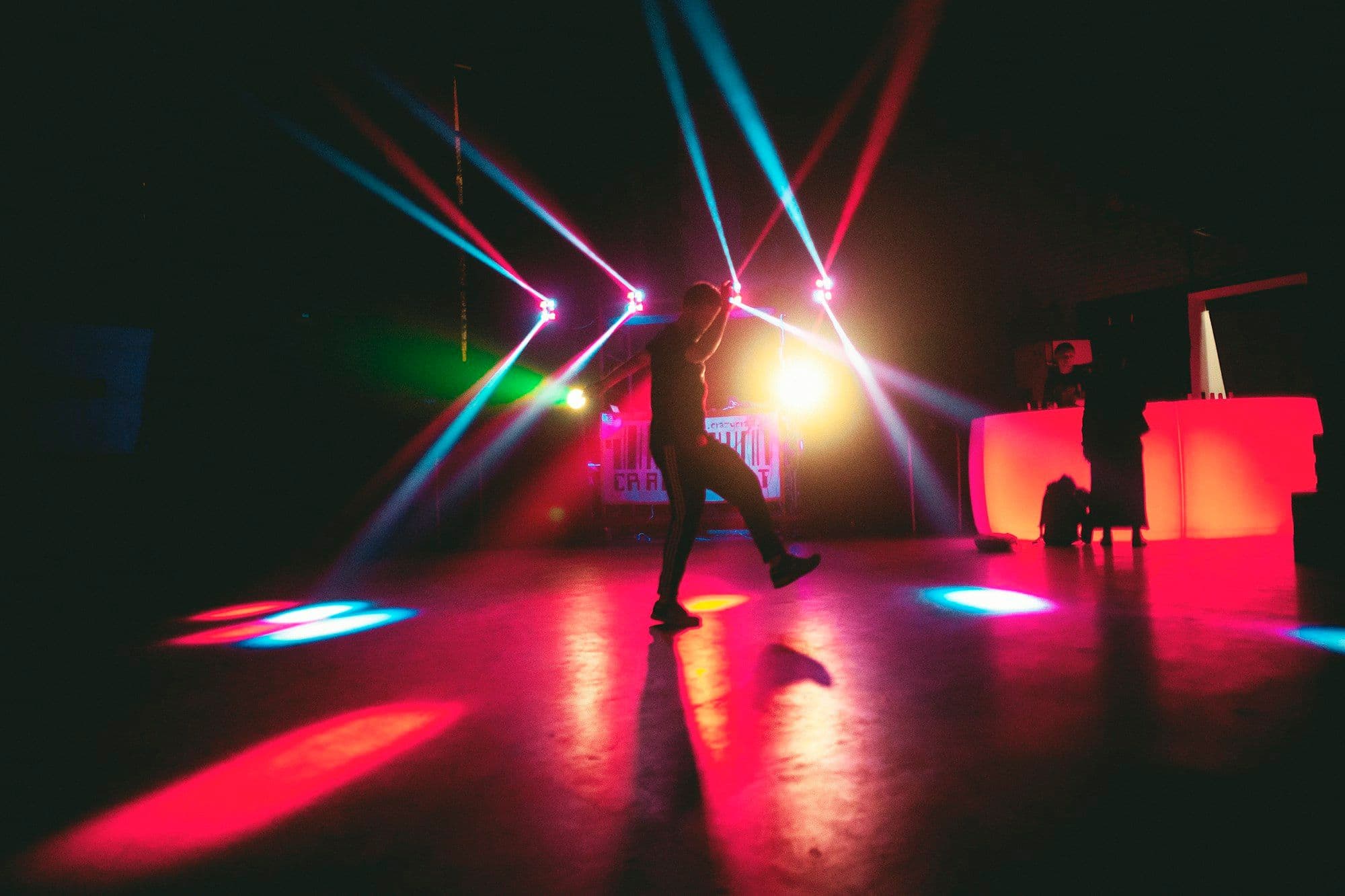 A lone dancer appears in silhouette beneath bright blue club lights.