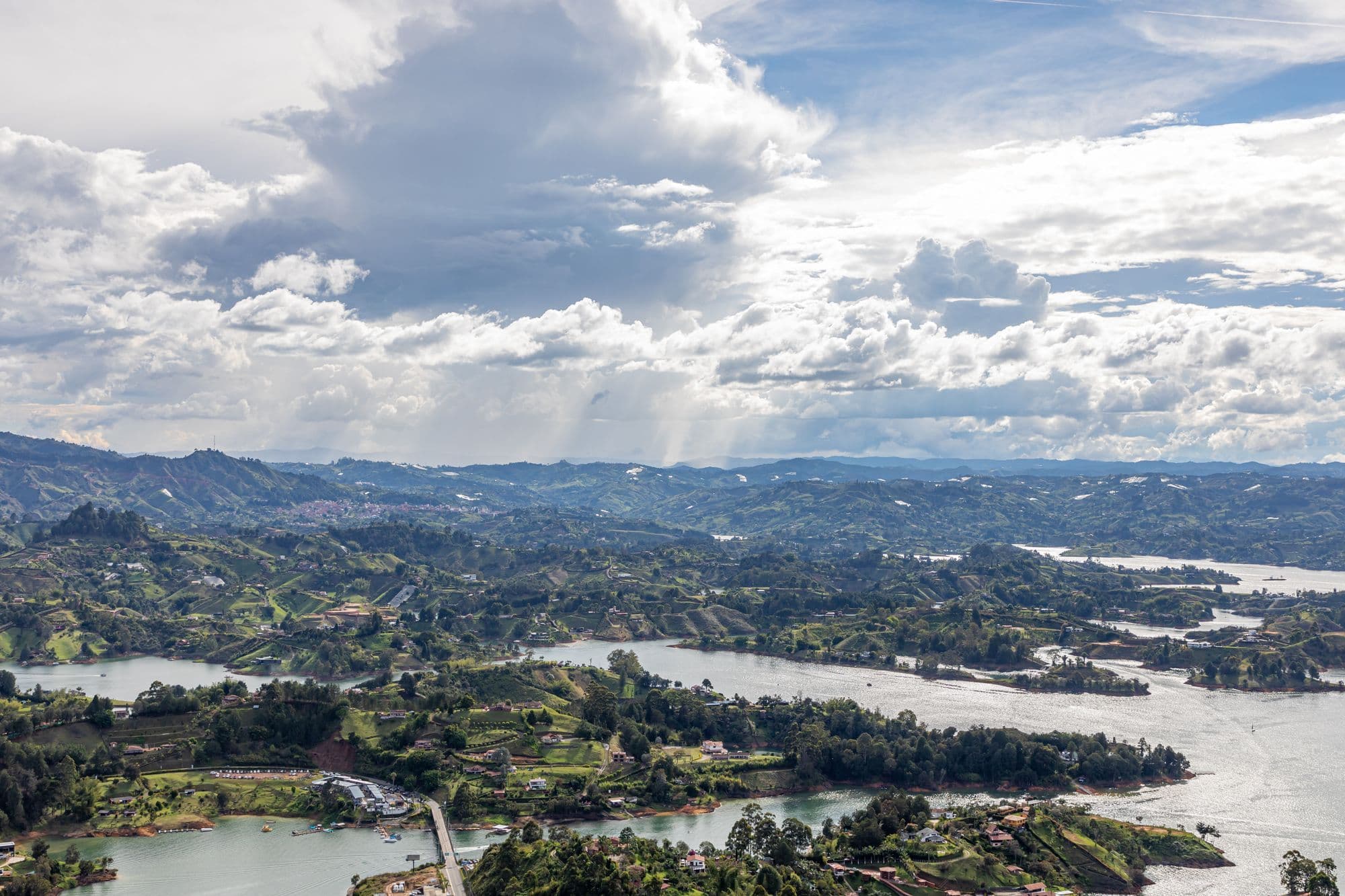 Aerial view over the winding lakes and green islands of the Guatapé reservoir under dramatic clouds.