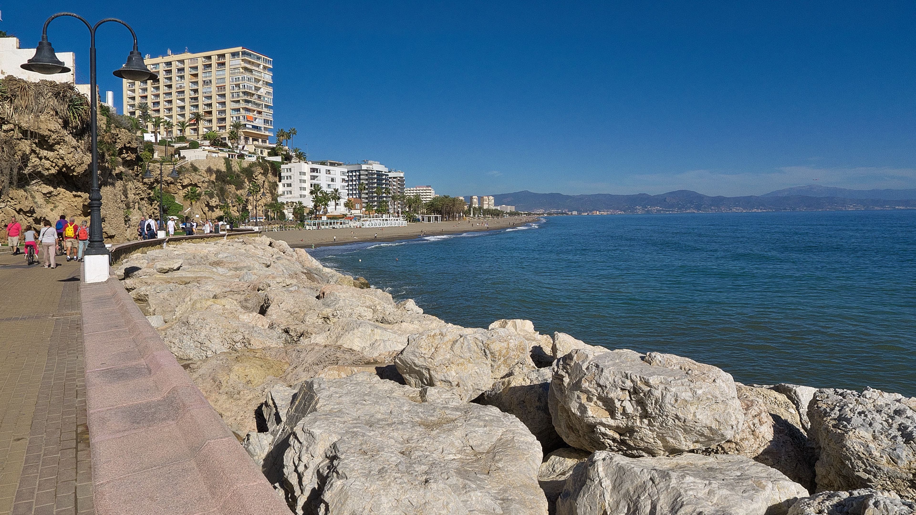 The promenade and rocky shore at Playa del Bajondillo in Torremolinos, with apartment blocks on the cliff and the coast curving away.