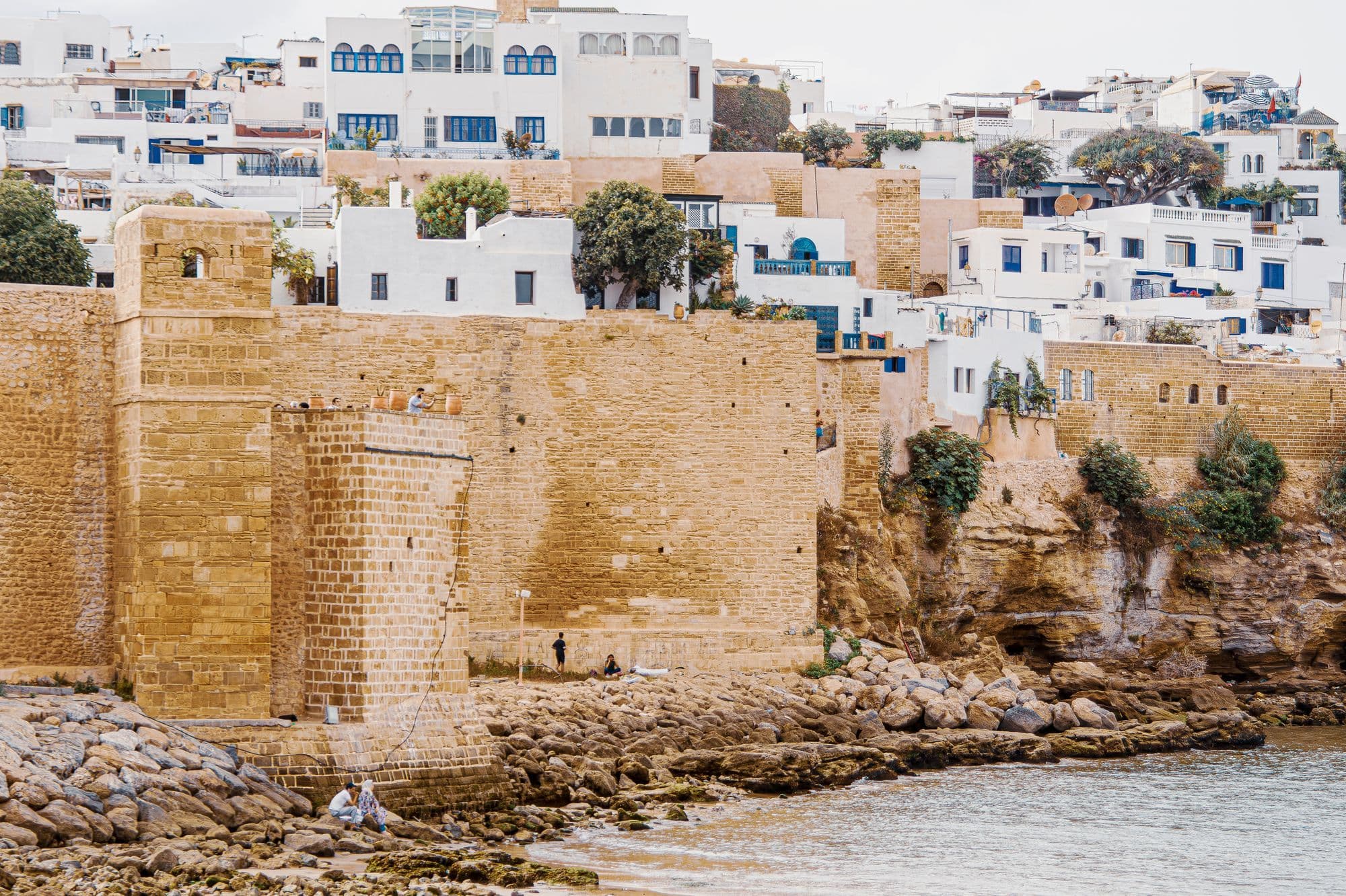 The ochre walls and square tower of the Kasbah of the Udayas above rocks, with white houses climbing the hill behind.